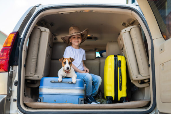 Happy boy in a cowboy hat and puppy jack russell terrier travel by car. A child and a funny little dog are sitting in the trunk and are ready for summer vacation. Independent travel. Best friends. Ταξίδι με τον σκύλο